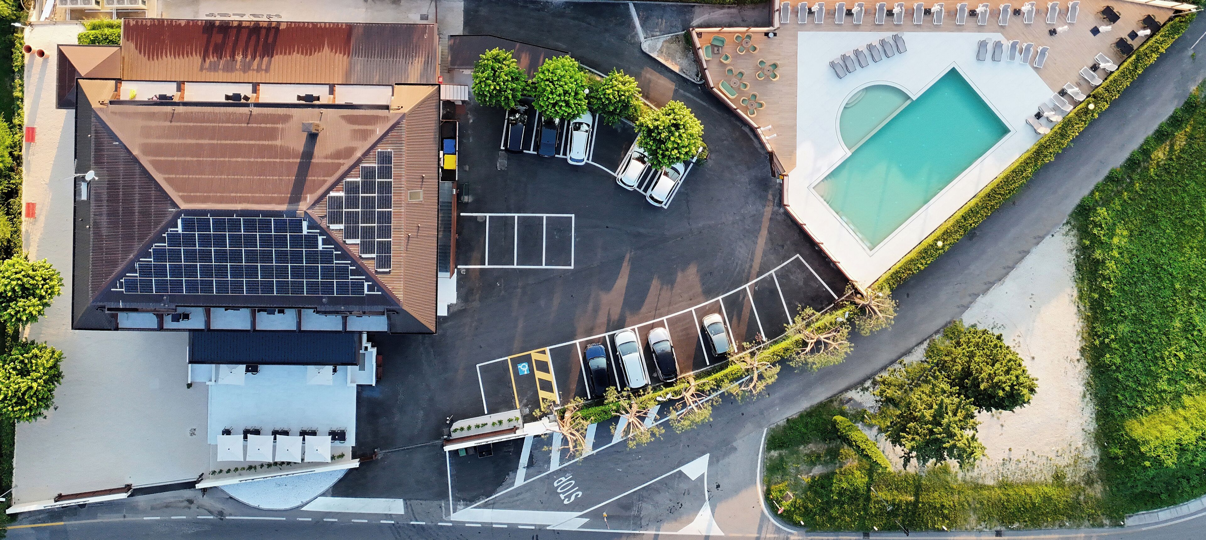 An aerial view of a hotel with a swimming pool, parking lot, and solar panels on the roof.
