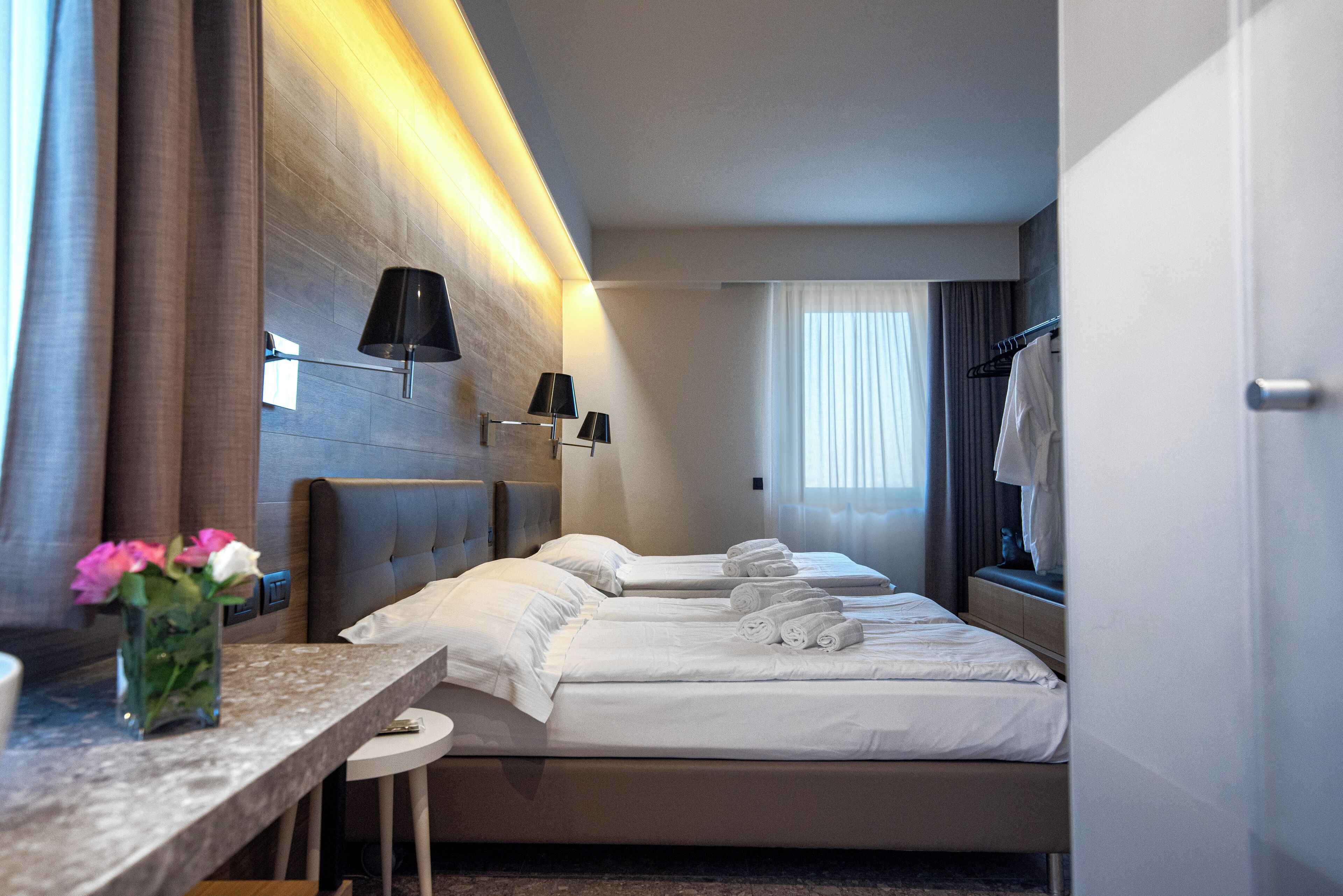 A hotel room with a bed, bedside tables, a desk, and a vase of flowers.