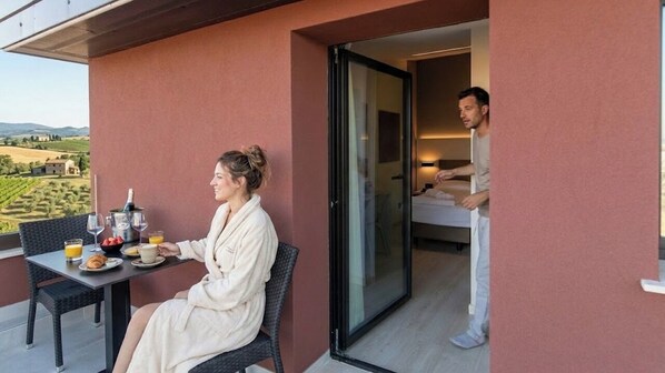 Un balcon avec une table préparée pour le petit-déjeuner, une personne assise et une autre debout près de la porte.
