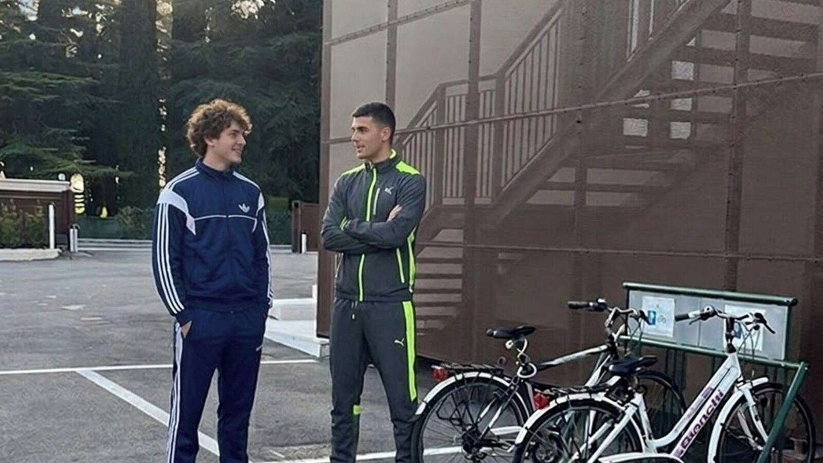 Two people standing in front of a building with bicycles parked nearby.