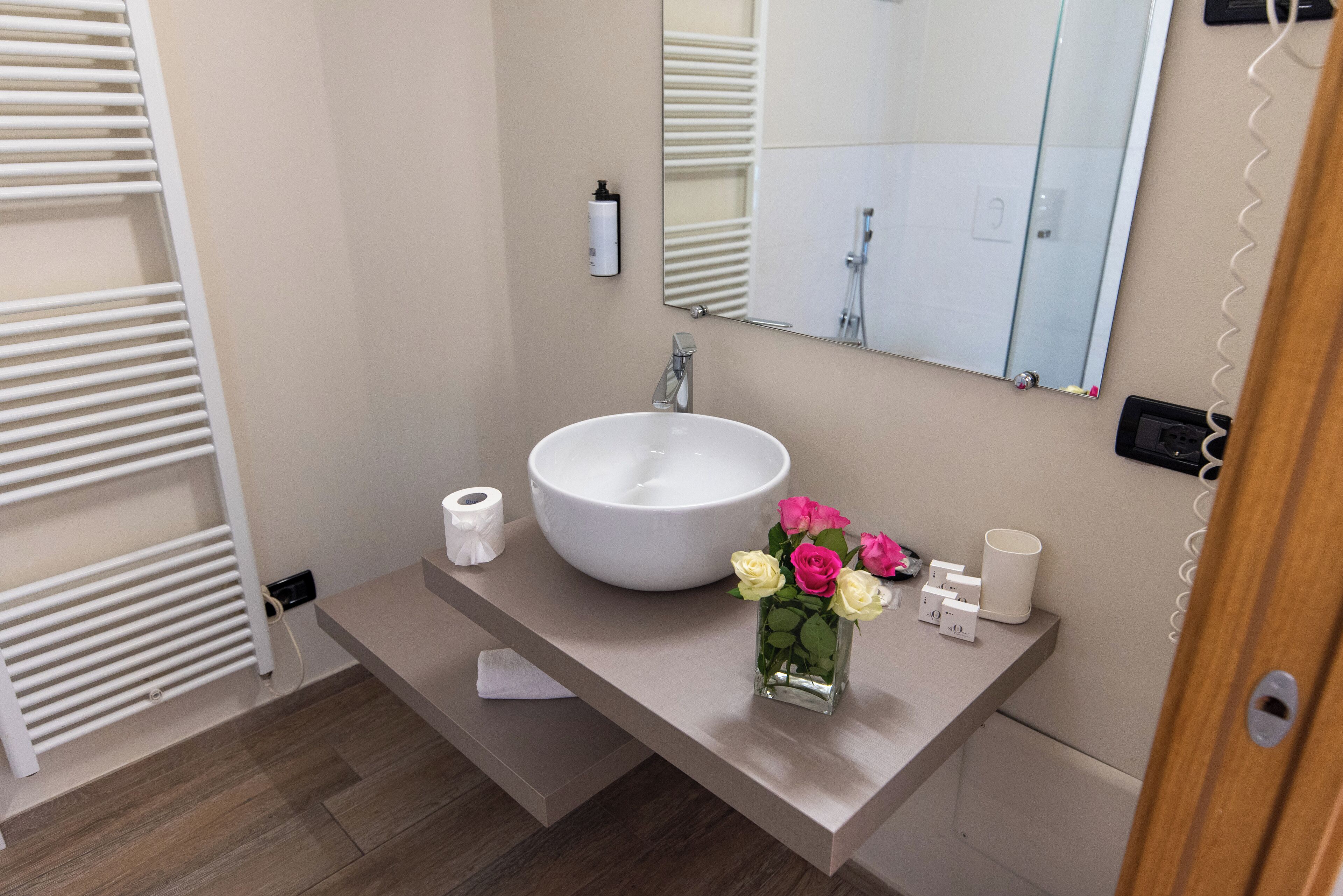 A modern bathroom with a large white sink, a mirror, a towel rack, and a vase with flowers.
