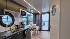 A modern kitchen with a black countertop, stainless steel appliances, and a view of the city through large windows. - Houseboat Fjord del Sol with bio sauna and roof terrace in Wendtorf / Kiel Fjord (Wendtorf)