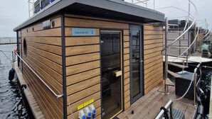A wooden boat with a deck, a small entrance, and a sign that reads "Fjord del Sol". - Houseboat Fjord del Sol with bio sauna and roof terrace in Wendtorf / Kiel Fjord (Wendtorf)