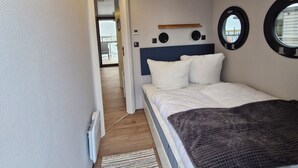 A bedroom with a bed, a window, a door, and a wall-mounted clock. - Houseboat Fjord del Sol with bio sauna and roof terrace in Wendtorf / Kiel Fjord (Wendtorf)