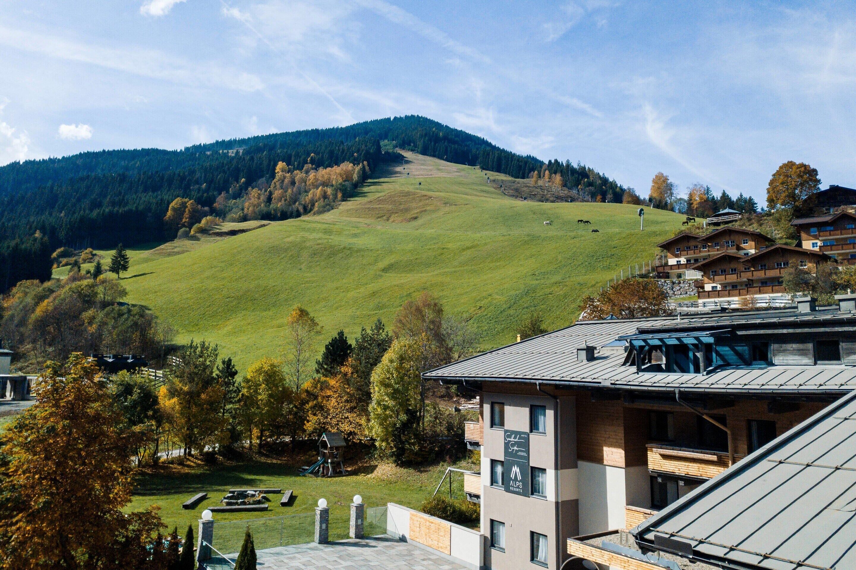 A hotel with a view of a green hill and forest.