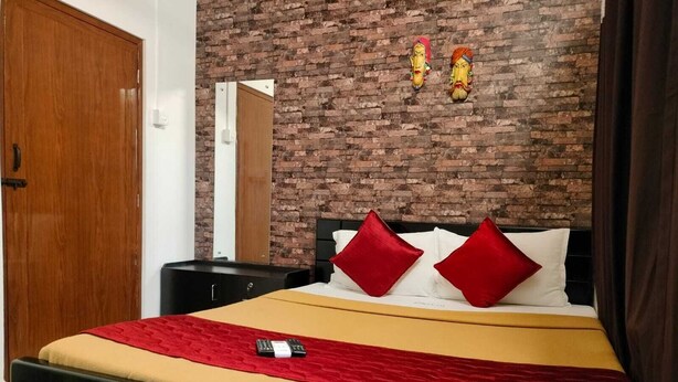 Una camera d'albergo con parete in mattoni, una porta in legno, un letto con cuscini rossi e bianchi e un comodino.