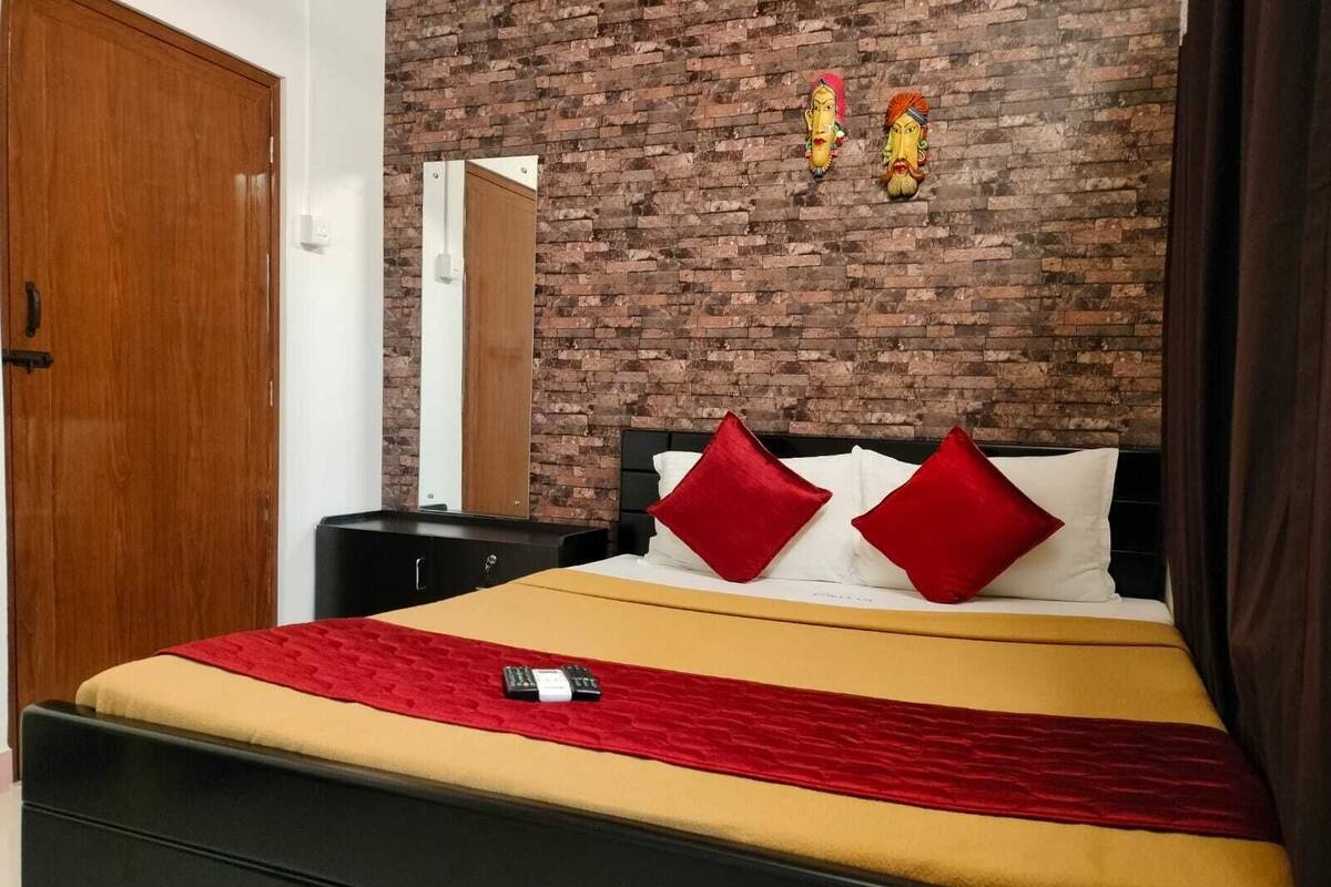 Una habitación de hotel con pared de ladrillo, puerta de madera, cama con almohadas rojas y blancas y una mesita de noche.