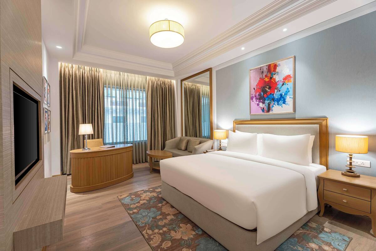 A hotel room with a large bed, a desk, a TV, and a painting on the wall.