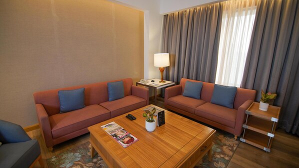 Habitación de hotel con dos sofás, una mesa de centro, una lámpara, una mesita auxiliar y una planta en maceta.