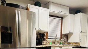 Une cuisine moderne dotée d’appareils électroménagers en acier inoxydable, de meubles blancs et d’un parquet en bois disposé en motif à chevrons.