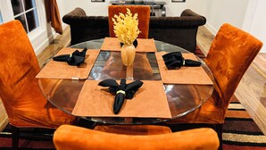 Une table à manger avec un plateau en verre, entourée de chaises en velours, un vase rempli de fleurs jaunes et des serviettes noires pliées, posées sur des sets de table.