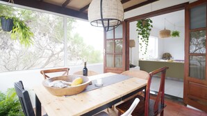 A dining area with a wooden table, chairs, hanging plants, and a view through a glass door. - Casa MaVi - Vineyard with ocean view  (pool, privacy, scenic views, BBQ, AC)  (Tinajo)