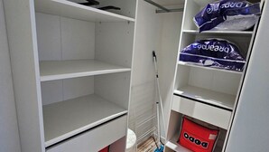 Ein weißer Kleiderschrank mit Regalen und Kleiderstange, der eine rote Tasche und eine blaue Tasche enthält.