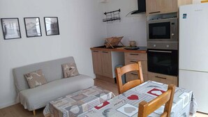 Ein gemütlicher Wohnbereich mit einer Couch, einem Esstisch mit Tischdecke, einem Holzstuhl, einer Küchenzeile mit Mikrowelle und einem Kühlschrank.