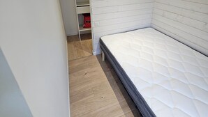 Ein Schlafzimmer mit einem Bett, Holzboden, einem weißen Kleiderschrank und einer kleinen roten Tasche.
