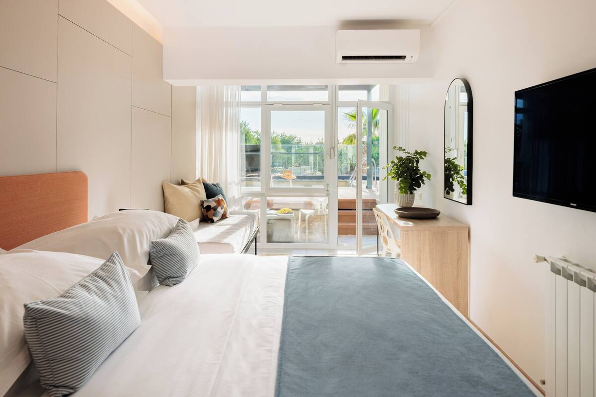 A modern hotel room with a large bed, a desk, a chair, and a balcony with a view.