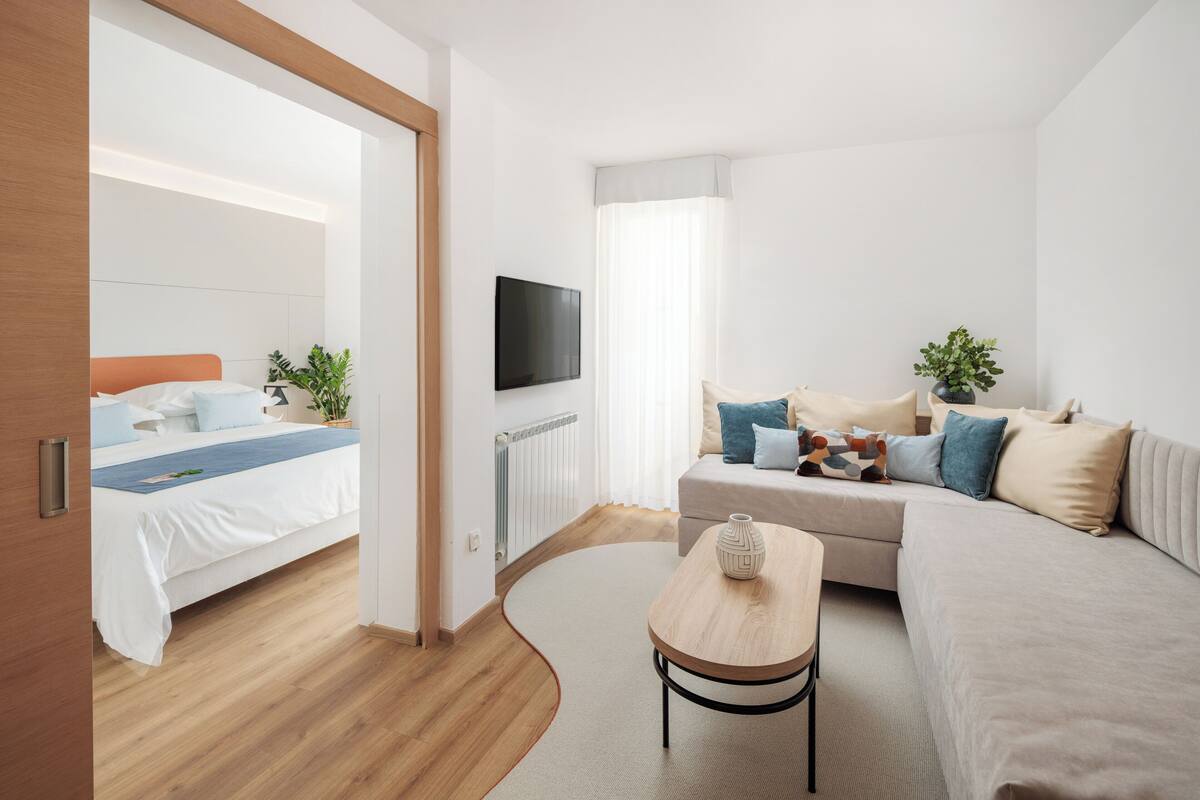 A modern hotel room with a bed, a sofa, a TV, and a small table.