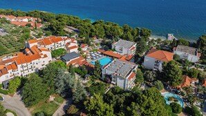 An aerial view of a coastal resort with multiple buildings, a swimming pool, and a view of the sea. - Hotel Waterman Kaktus (Supetar)