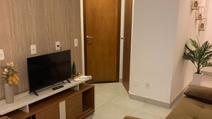 Ein modernes Wohnzimmer mit einem Flachbildfernseher auf einem Holz-TV-Schrank, einem Esstisch mit Stühlen, einem Sofa und einer Topfpflanze.
