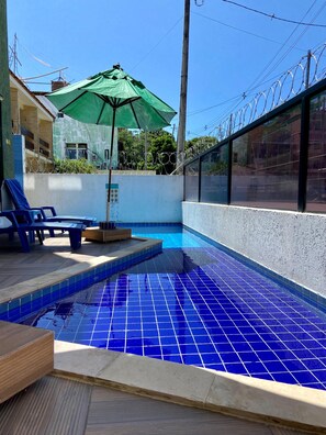 A swimming pool with blue tiles, a green umbrella, and a barbed wire fence.