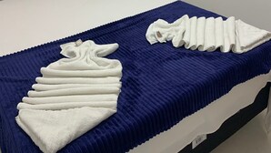 Ein Hotelzimmer mit einem ordentlich bezogenem Bett, einer blauen Decke und gefalteten Handtüchern auf dem Bett.
