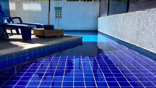 Ein Swimmingpool mit blauen Fliesen, einer Holzterrasse und einem grünen Sonnenschirm.
