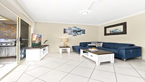 Una sala de estar moderna con un sofá azul, una mesa de centro, un televisor sobre un mueble bajo y una parrilla en el exterior.