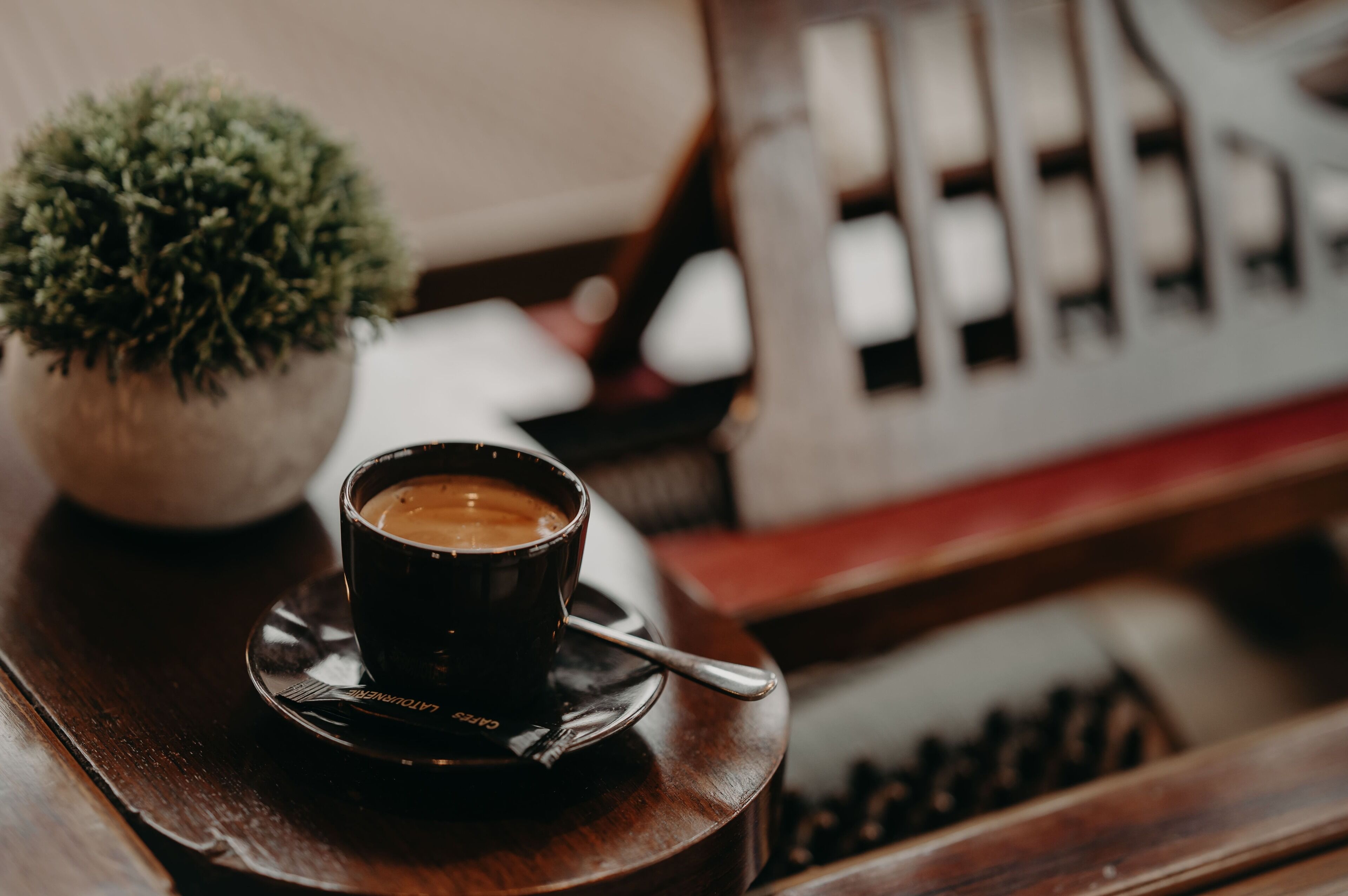 A cup of coffee on a saucer with a spoon, a small potted plant, and a wooden surface.