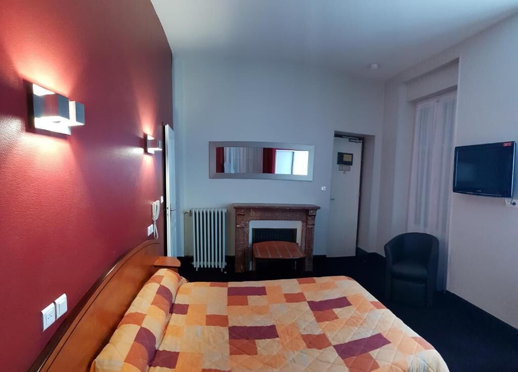 Una camera d'albergo con un letto, una poltrona, un camino, una TV e uno specchio a parete.