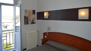 Een slaapkamer met een bed, een radiator, een telefoon en een wandlamp.