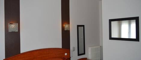 Hotellihuone, jossa on parivuode, yöpöytä, peili ja seinään kiinnitetty valaisin.
