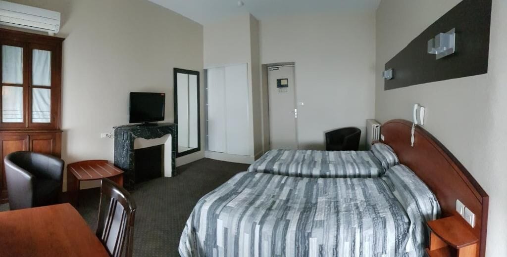 Habitación de hotel con una cama, un escritorio, una silla, un televisor y un armario.