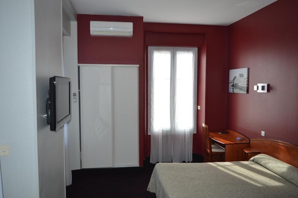 Une chambre d’hôtel avec un lit, un bureau, une chaise, une télévision et une fenêtre avec des rideaux.