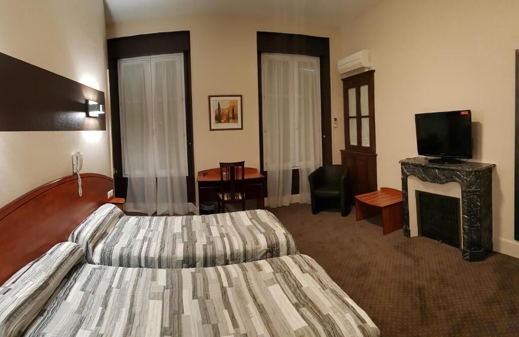 A hotel room with a bed, a desk, a chair, a television, and a fireplace.