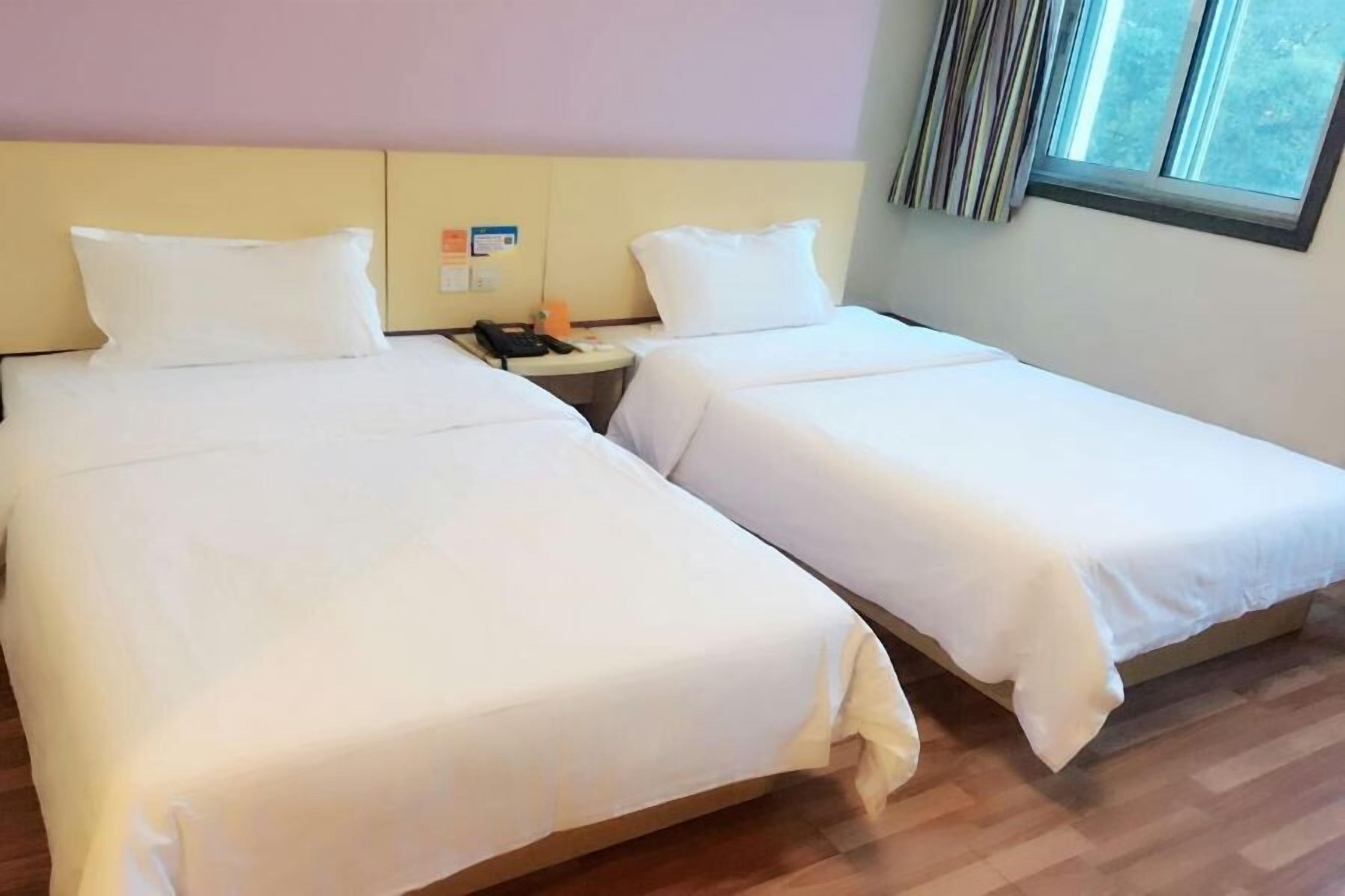 Two single beds with white linens in a room with wooden flooring and a window with blinds.