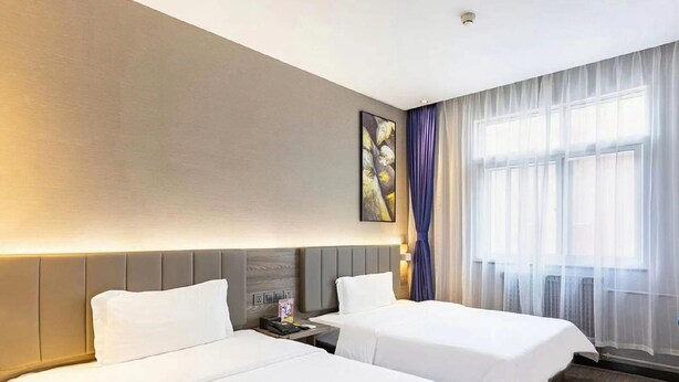 Ein Hotelzimmer mit zwei Betten, einem großen Fenster mit durchscheinenden Vorhängen, einem Bild an der Wand und einer modernen Leuchte.