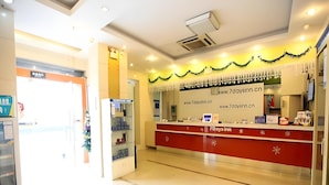 Ein Hotel-Rezeptionsbereich mit einem roten Empfangstresen, einer weißen Wand mit einer Website-Adresse und einem Glastür-Eingang.