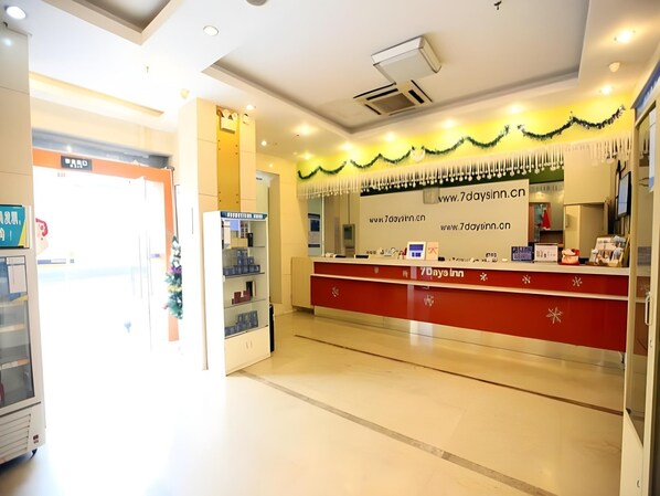 A hotel reception area with a red counter, a white wall with a website address, and a glass door entrance.