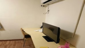 Ein kleiner Raum mit Holzboden, einem Schreibtisch mit Flachbildfernseher, einem Stuhl und einer Plastiktüte auf dem Schreibtisch.