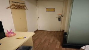 Ein Flur mit Holzboden, einem Schreibtisch mit Tasche und Buch, einem Kleiderständer und einer Tür mit einem Schild.