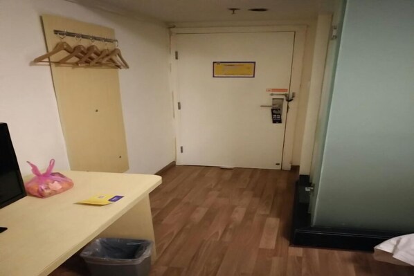 A hallway with a wooden floor, a desk with a bag and a book, a coat rack, and a door with a sign.