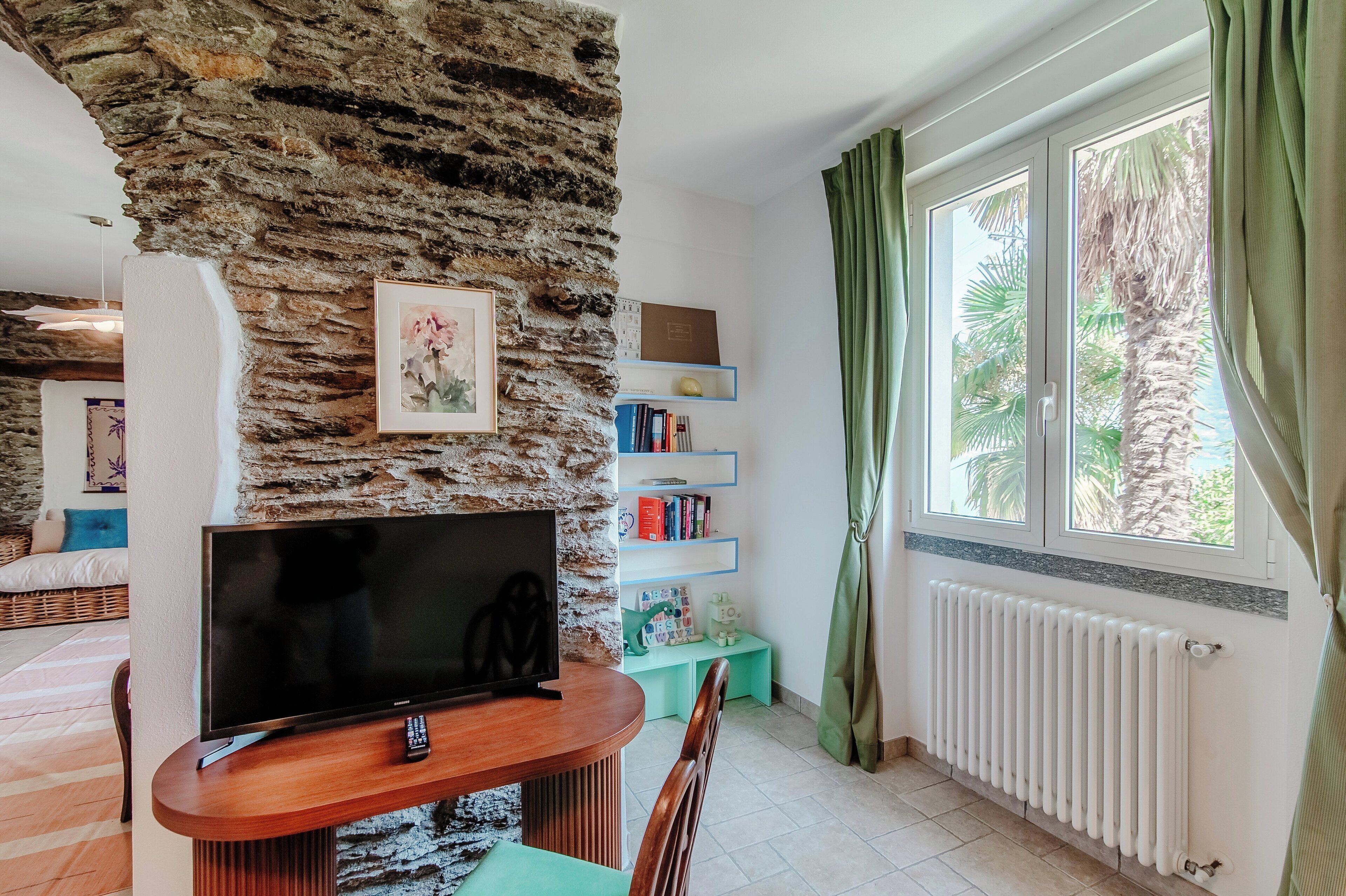 Een woonkamer met een stenen muur, een flatscreen televisie, een boekenkast en een raam met gordijnen.