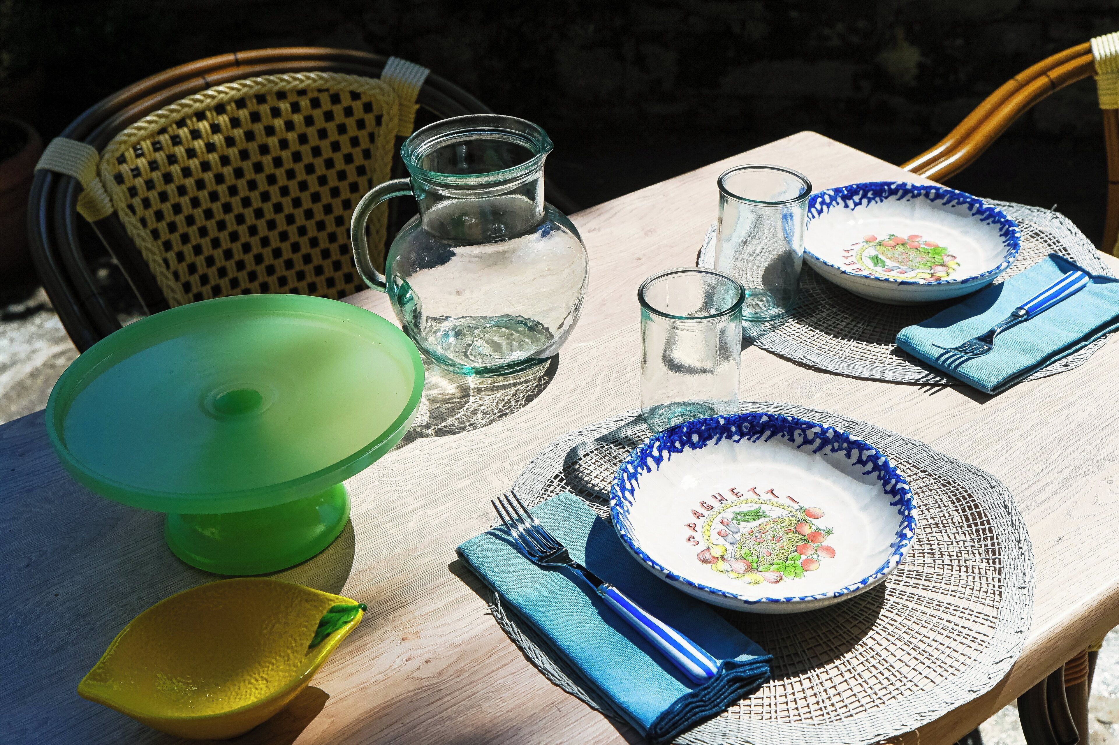 Une table dressée avec des assiettes, un pichet, des verres et un récipient vert, probablement destiné à servir les aliments.