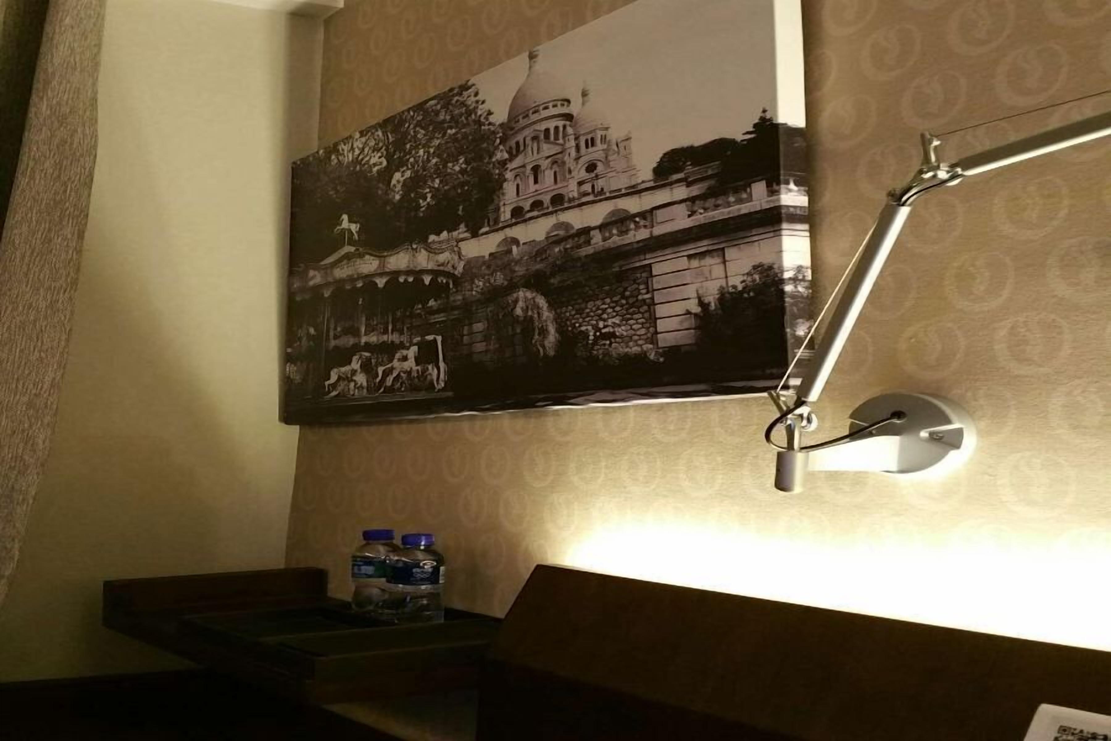 A bathroom with a wall-mounted picture of a historical building, a mirror, and a bottle of water on the counter.