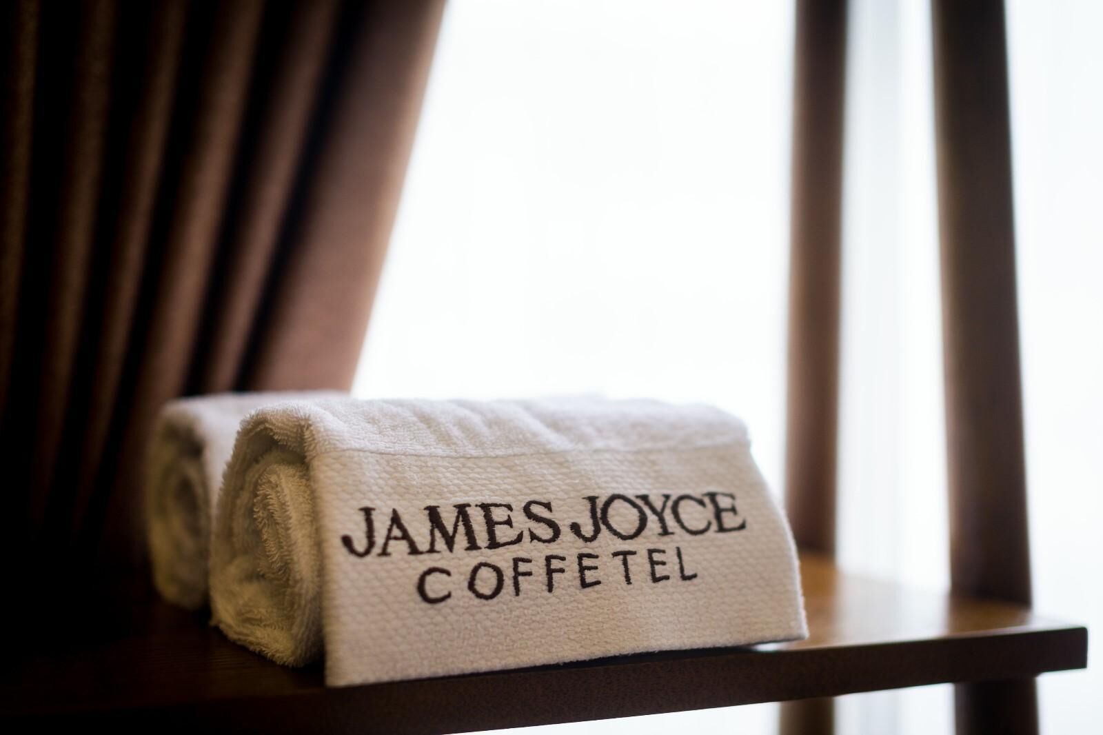 A neatly folded towel with the name 'James Joyce Coffetel' on a wooden chair.