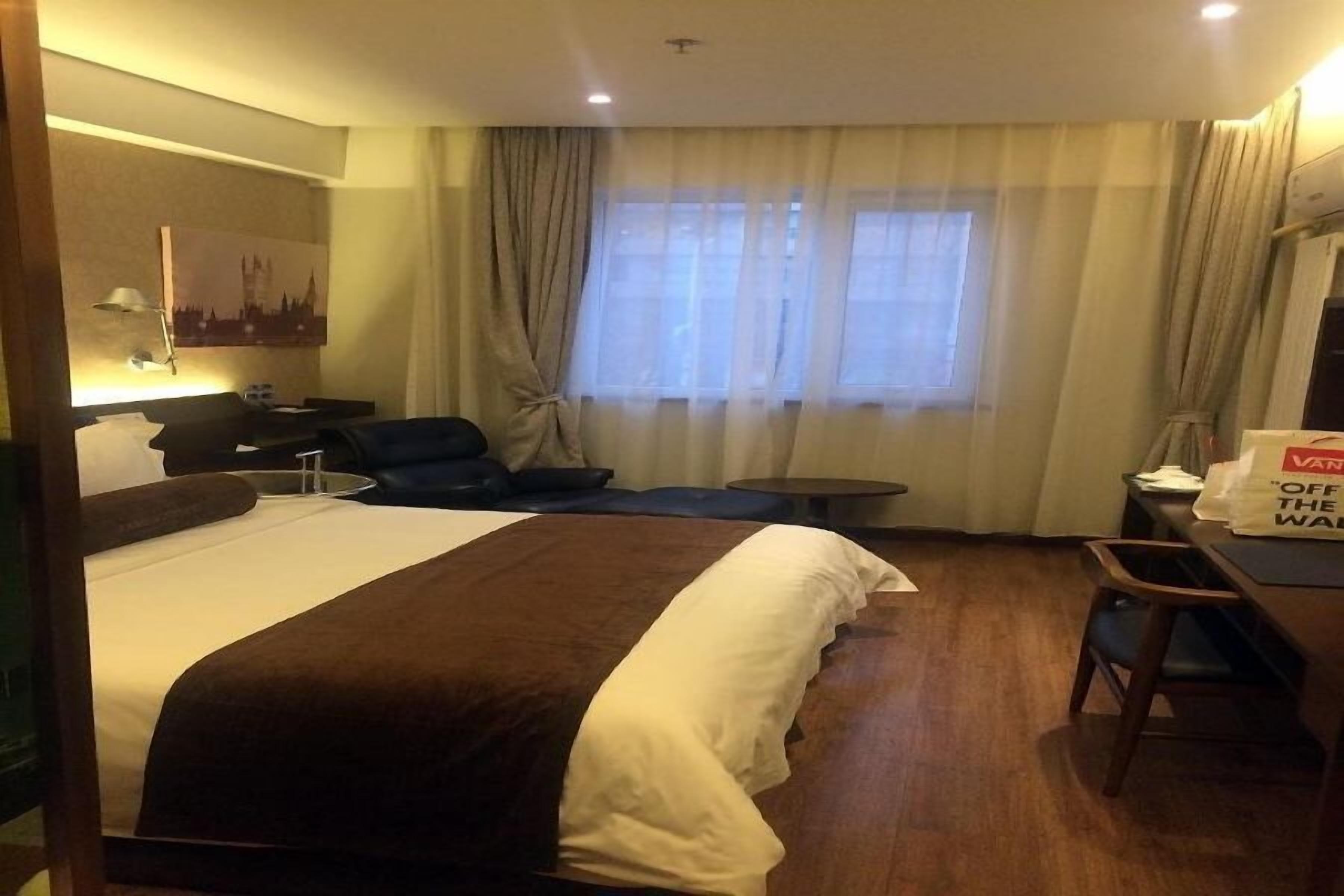 A hotel room with a large bed, a desk, a chair, a sofa, and a window with curtains.