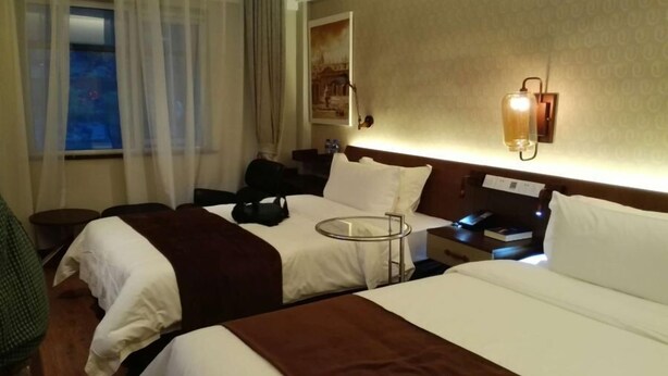 Hotelkamer met twee bedden, een bureau, een stoel, een raam met gordijnen en een wandlamp.