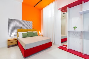 A modern bedroom with a red and white color scheme, a bed with green pillows, a nightstand with a lamp, and a white wardrobe with a plant on top. - Starguest Duomo  (Naples)