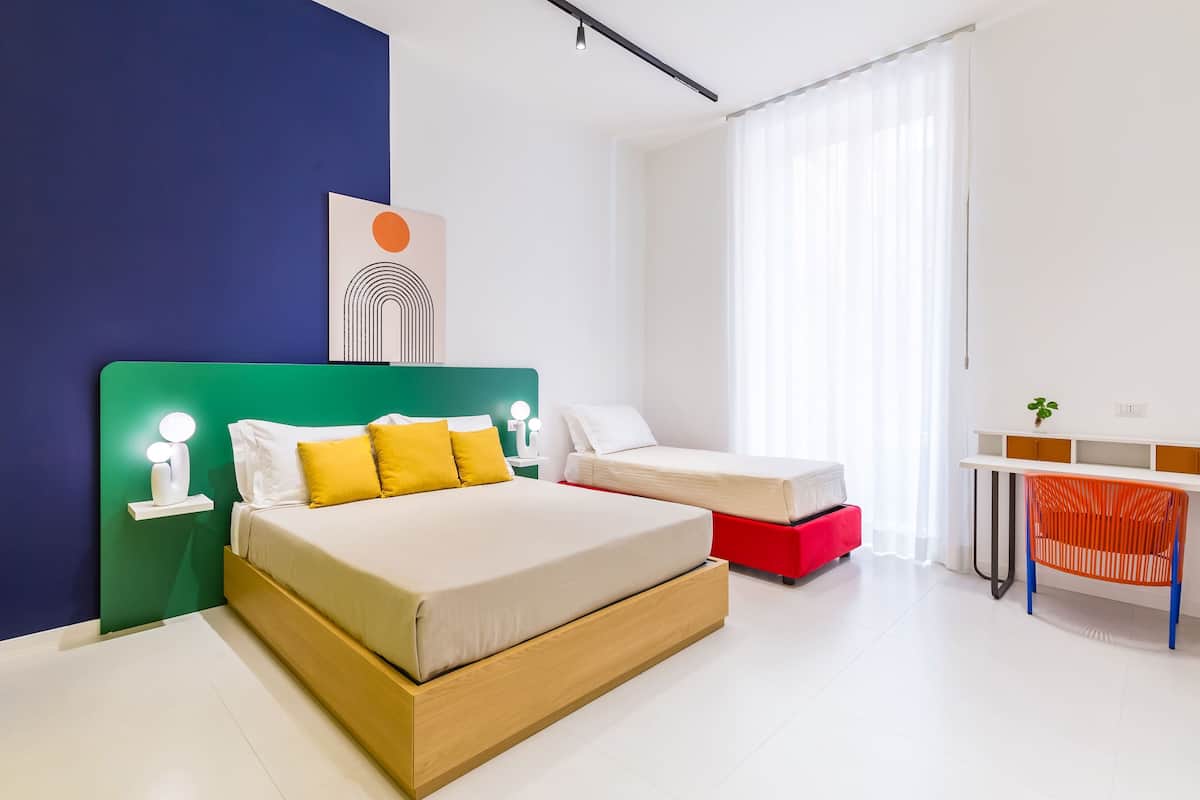 A modern bedroom with a large bed, a smaller bed, a desk, and a chair.