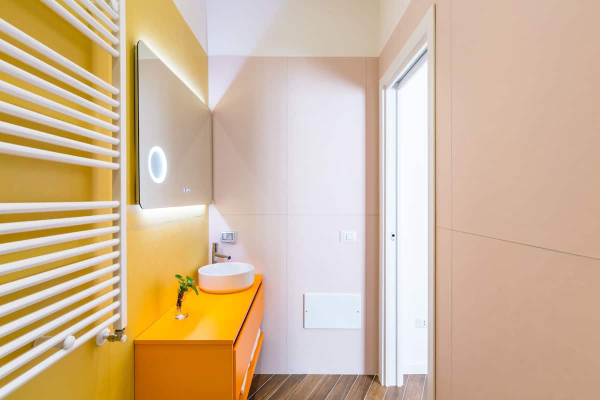 A modern bathroom with a yellow vanity, a white sink, and a mirror with a light.